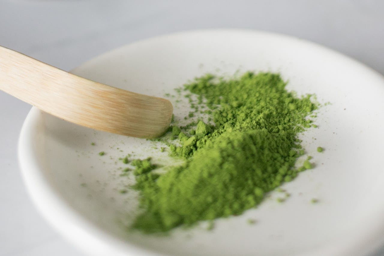 Vibrant green matcha powder on a ceramic plate with wooden spatula in a minimalist setting.