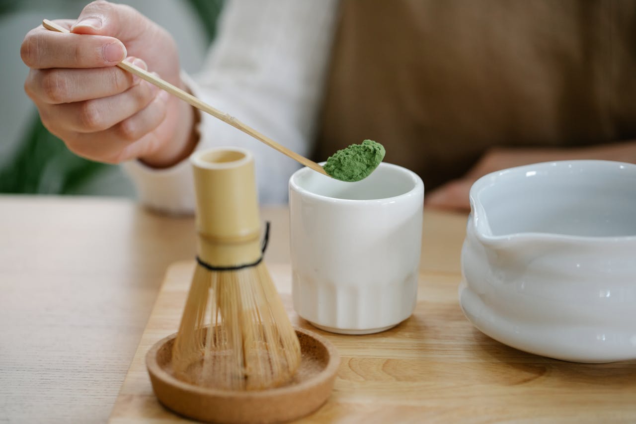 A person prepares matcha tea using traditional tools on a wooden table.